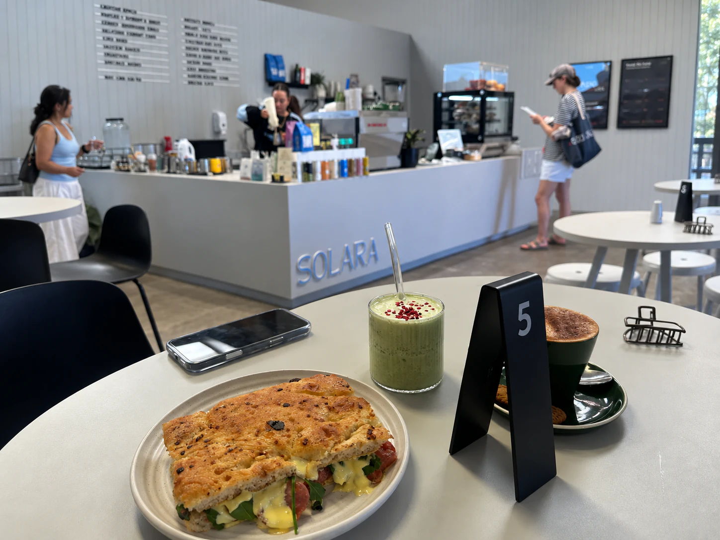 A cafe table with a sandwich, coffee and a green drink